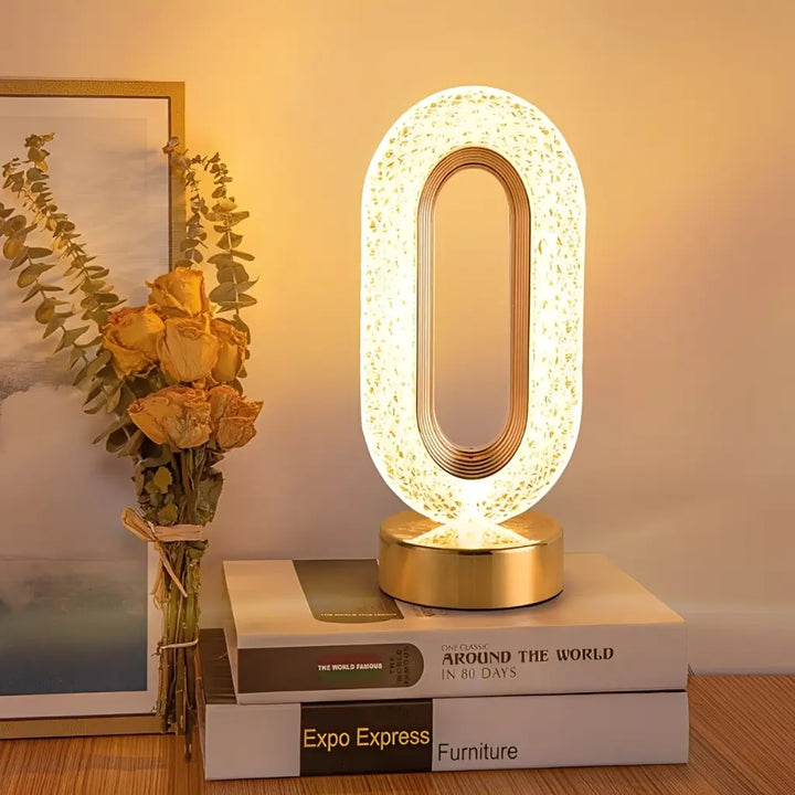 luminaria-de-mesa-dourada-acrilico-cristal-acesa-com-luz-quente-em-sala-com-decoracao-moderna-e-livros-decorativos-com-design-sofisticado